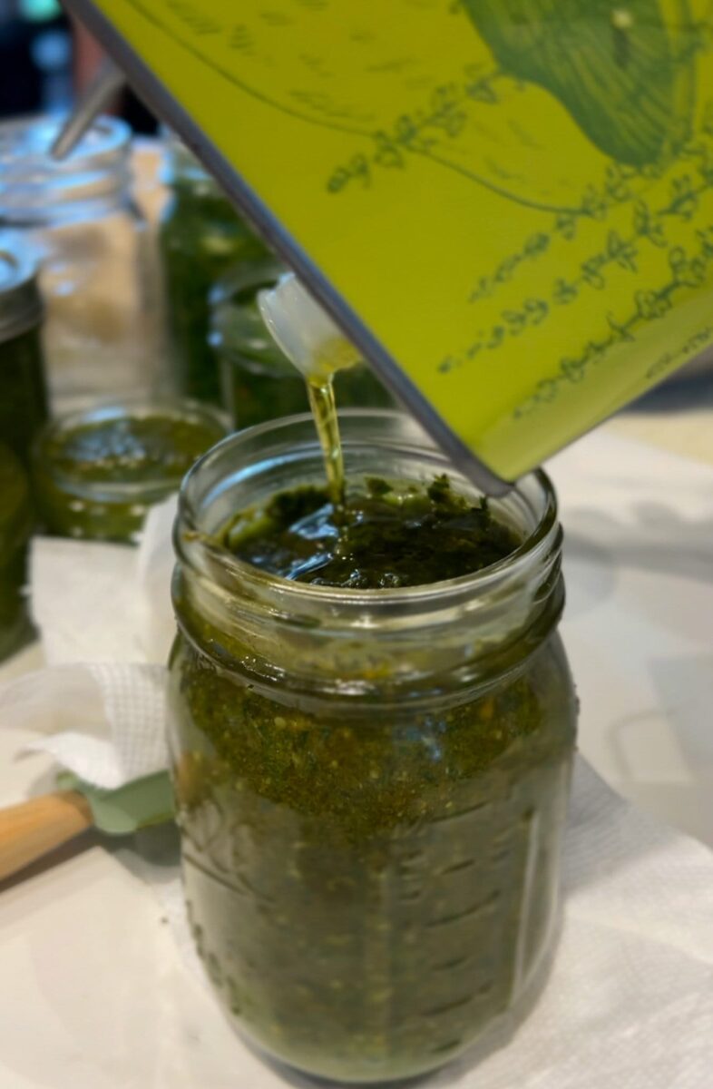 bidon d'huile d'olive qui verse une couche d'huile sur le dessus d'un pot de pesto maison