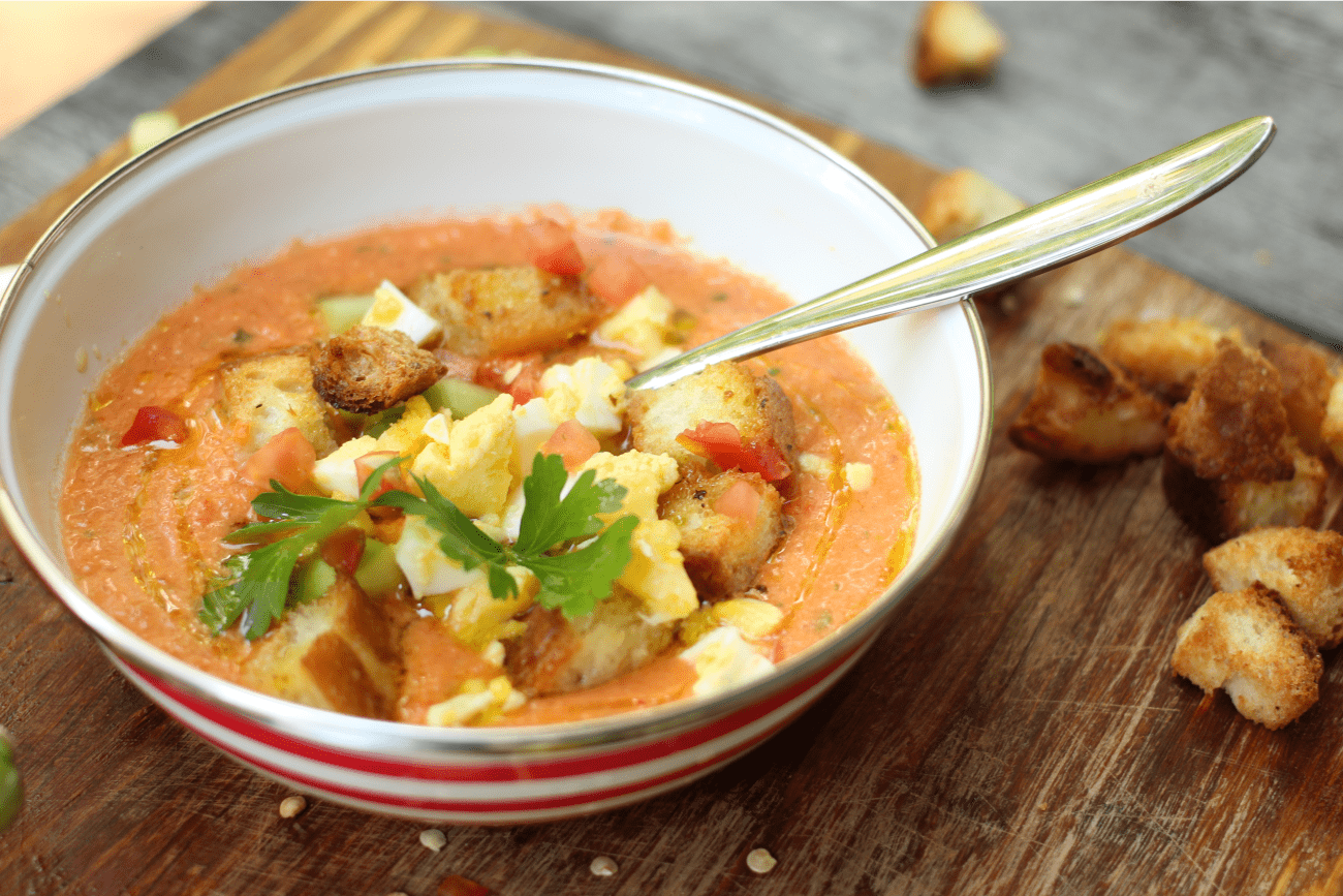 soupe gaspacho dans un bol blanc, garni d'oeuf en dés, herbes et croûtons