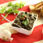 tapenade noire dans un petit bol blanc avec pain grillé et tête d'ail