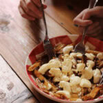 Poutine maison dans un bol, deux mains avec fourchettes qui pigent dans le bol