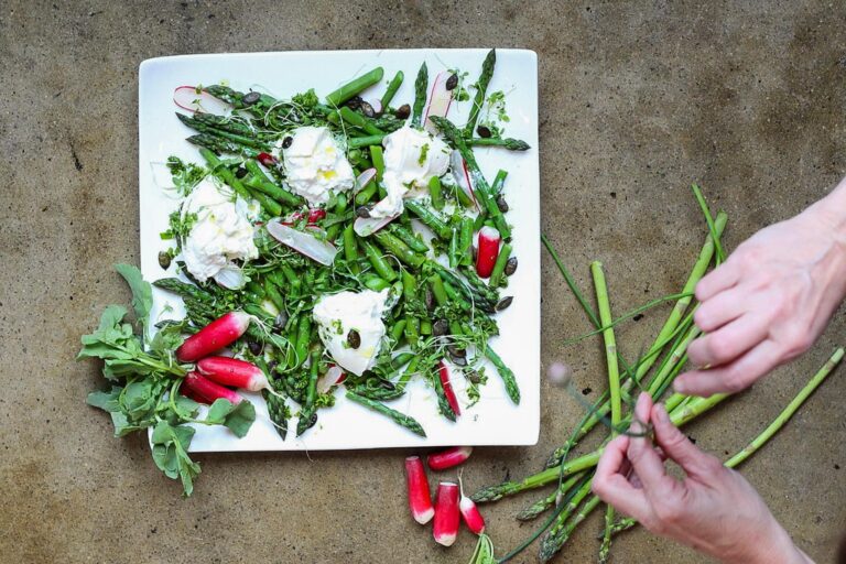 salade d'asperges et burrata avec radis et mains qui déposent des herbes et asperges dans l'assiette