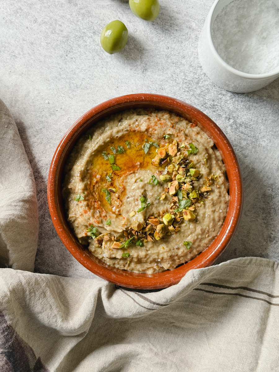 baba ganoush aux pistaches dans plat en terre cuite avec olives sur le côté et pot de fleur de sel