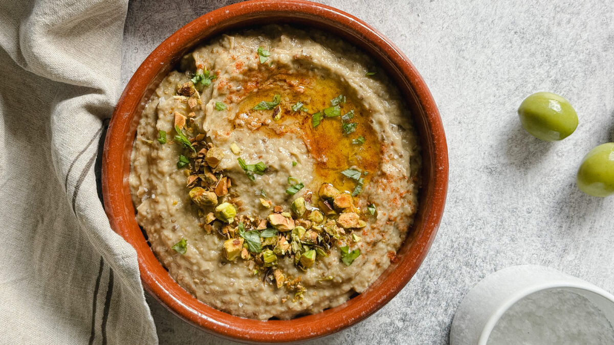 baba ganoush dans un plat en terre cuite sur surface beton avec 2 olives vertes et pot de fleur de sel