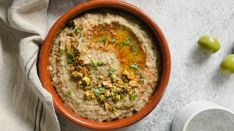 baba ganoush dans un plat en terre cuite sur surface beton avec 2 olives vertes et pot de fleur de sel
