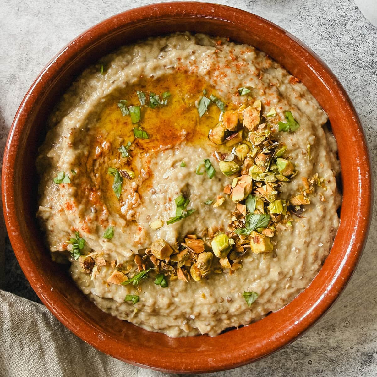 baba ganoush avec garniture de pistaches, huile d'olive et paprika dans petit plat en terre cuite