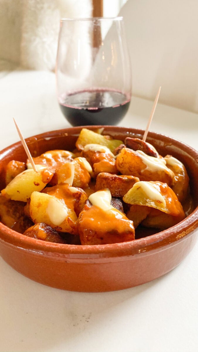 plat en terre cuite remplie de patatas bravas avec sauce rouge et blanche et petits cure dents, coupe de vin rouge en arriere plan