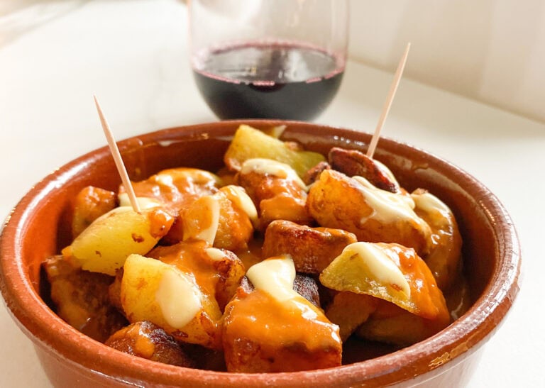 plat de patatas bravas avec sauce brava et mayonnaise, coupe de vin rouge en arrière plan