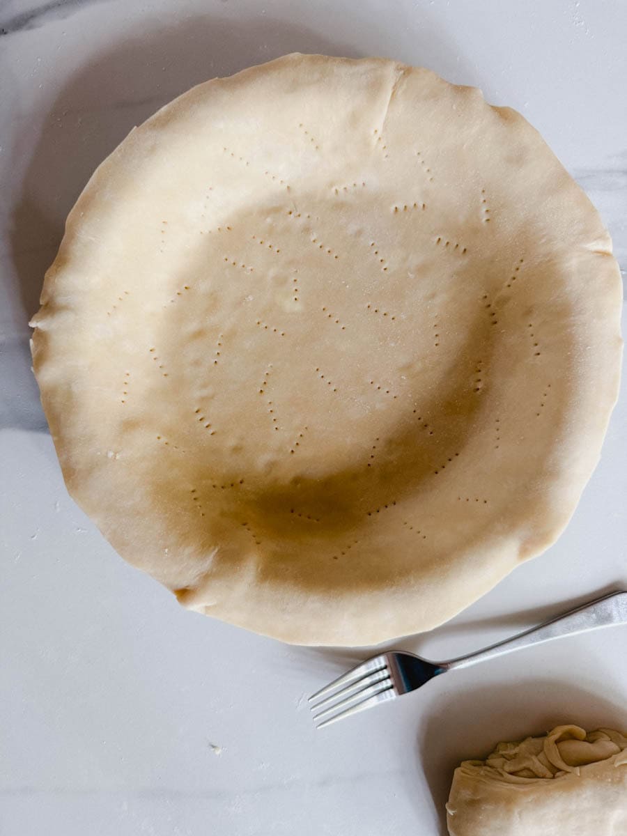 abaisse de pâte à tarte dans moule à tarte avec fourchette et marques sur comptoir