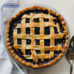 tarte aux bleuets avec cuillère de service et linge en lin blanc sur comptoir pâle