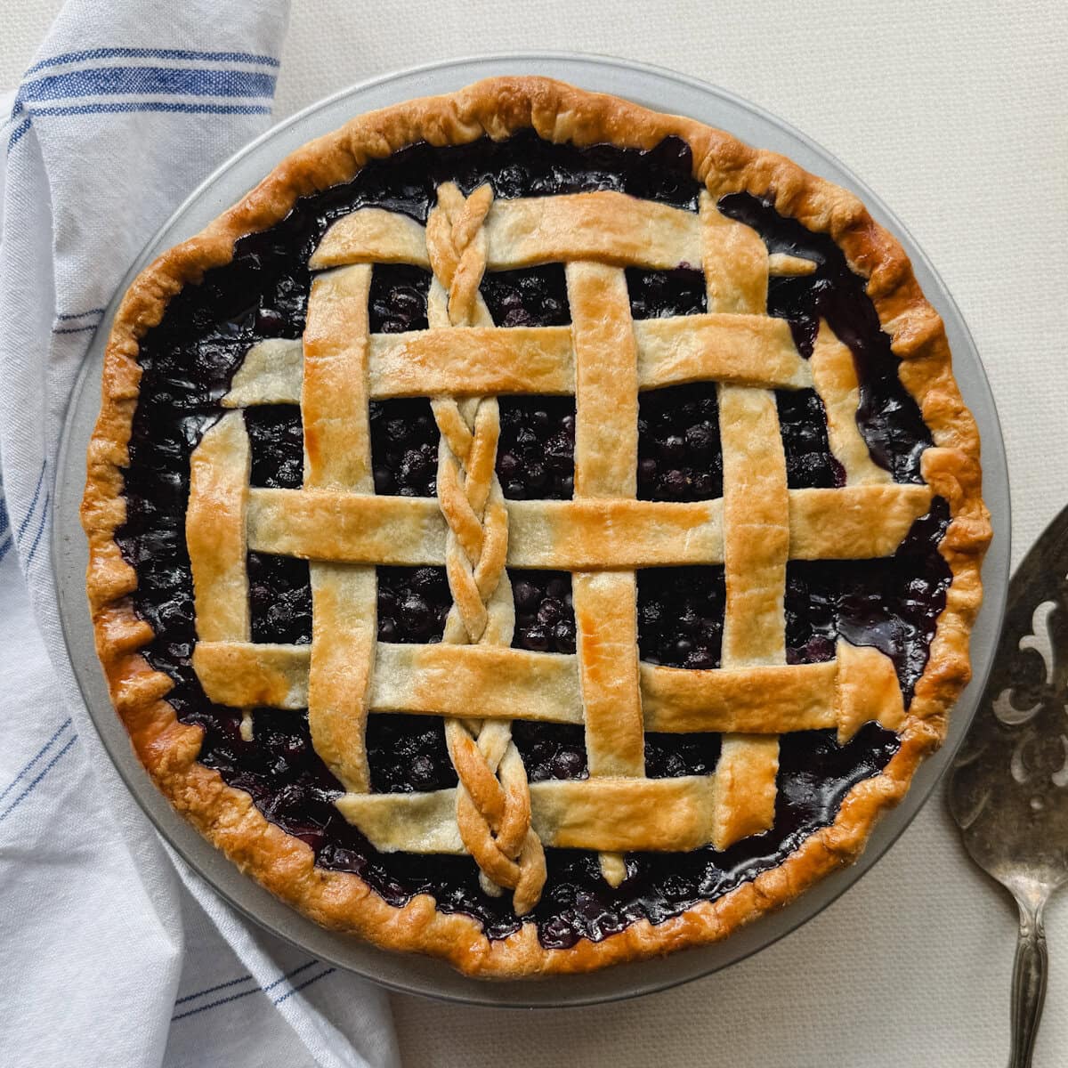 tarte aux bleuets avec cuillère de service et linge en lin blanc sur comptoir pâle