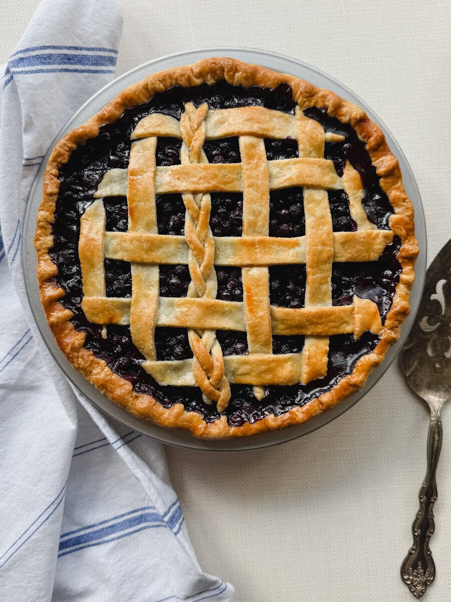 tarte aux bleuets traditionnelle, bien grillée, avec spatule e service et linge de lin sur comptoir pâle