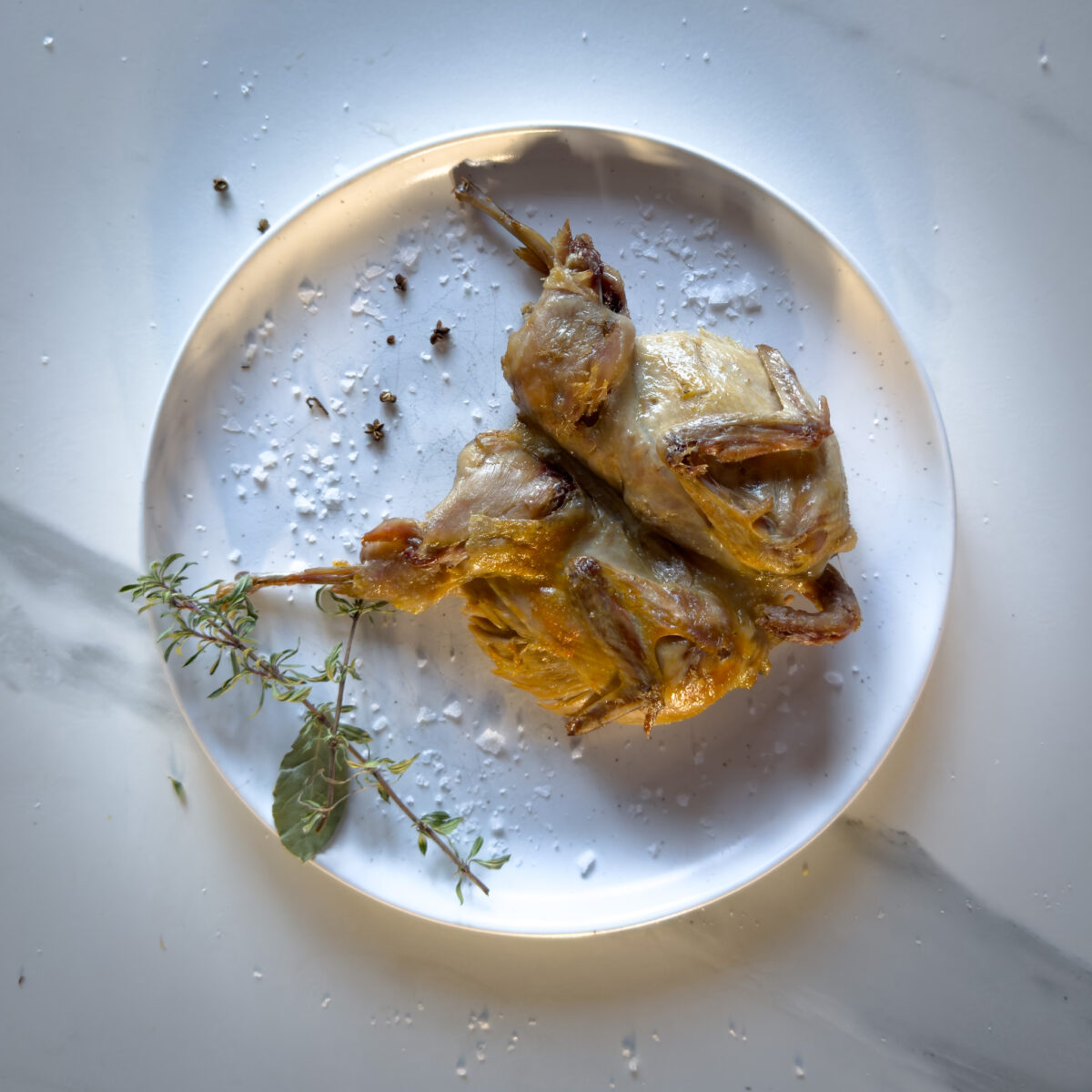 caille confite dans une assiette blanche avec fleur de sel et herbes