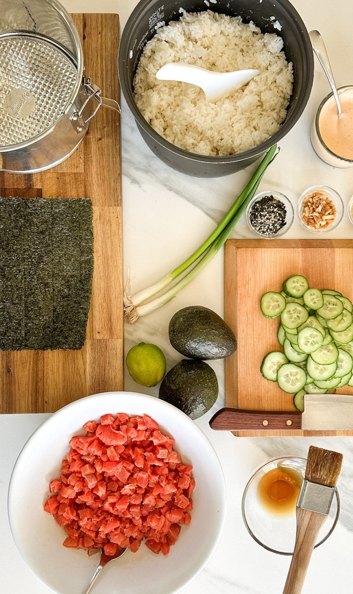 Ingrédients pour gateau sushi: saumon, concombre, avocat, riz sushi, furikake, algue nori sur un comptoir 