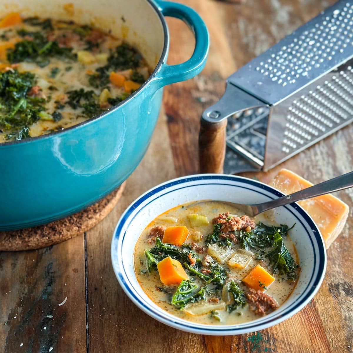 bol de soupe toscane aux légumes et saucissse avec casserole de soupe et râpe à fromage en arrière-plan