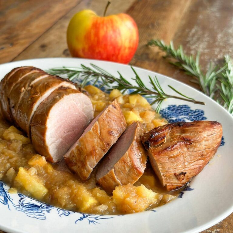 filet de porc grillé sur une sauce compote de pomme dans une assiette avec branche de romarin et pomme en arrière plan