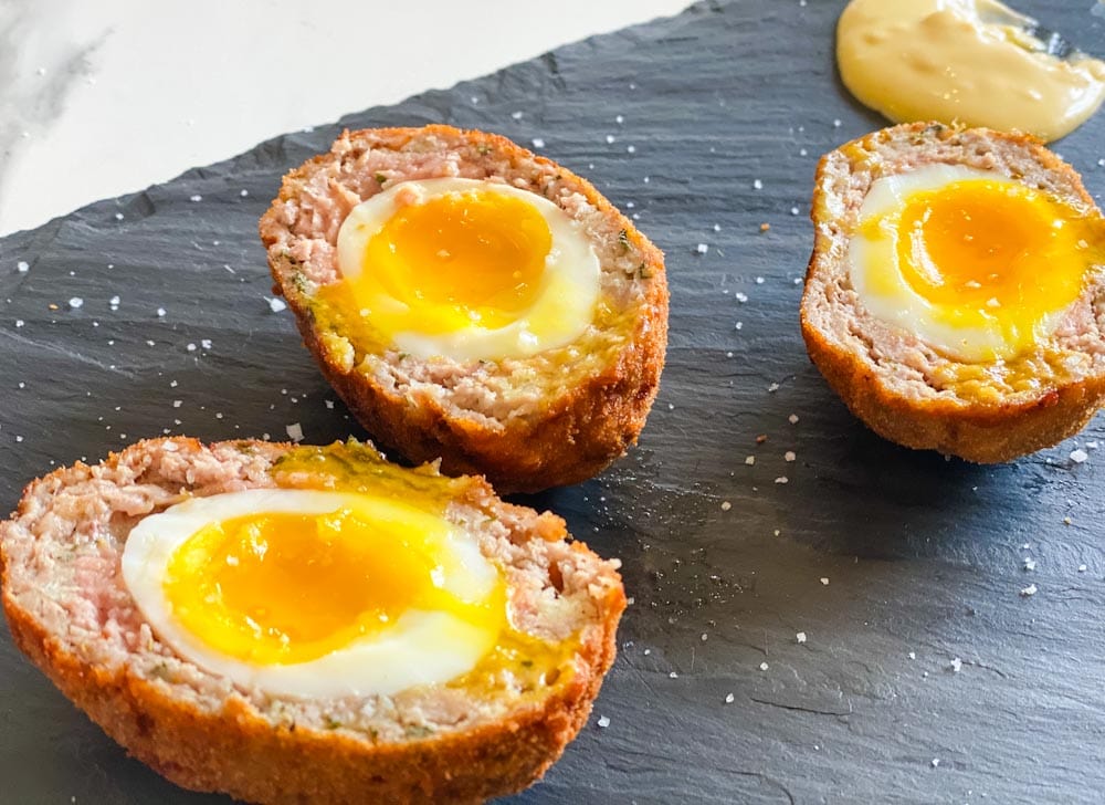 oeuf écossais scotch eggs ouverts sur une planche de service, jaune coulant, cuisson parfaite