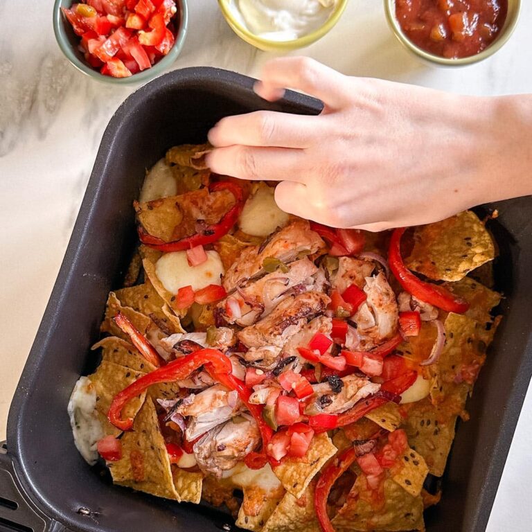 main qui prend des nachos au poulet dans le panier du air fryer