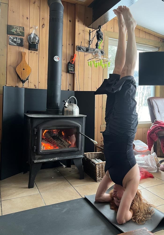 Manon Lapierre qui fait du yoga posture sur la tête dans un chalet devant un foyer