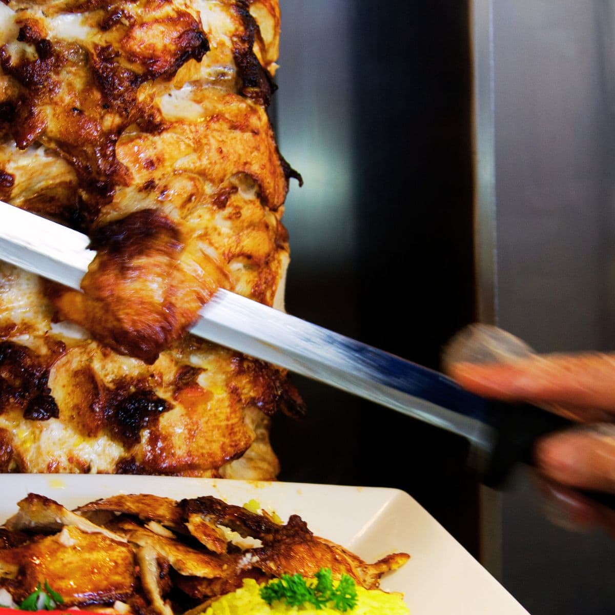 shawarma de poulet grillé, main ganté qui coupe au couteau dans une assiette