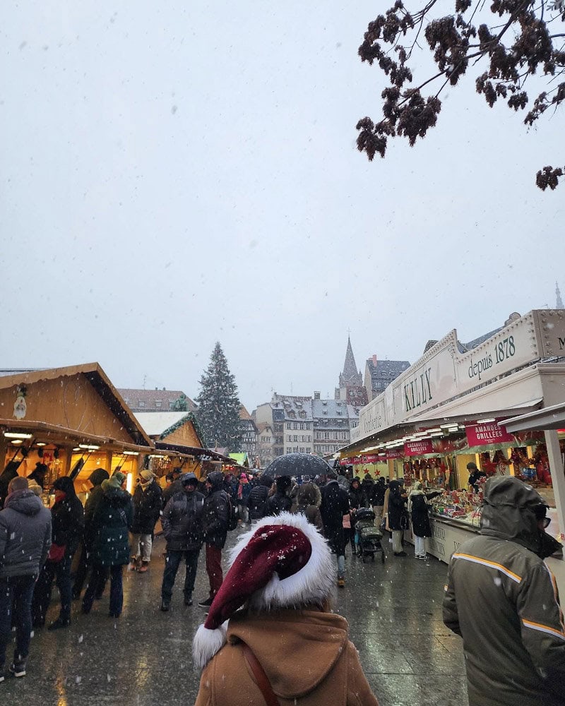 marché de noël place Kleber de jour sous la neige, femme de dos avec chapeau de Noël