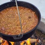 fèves au lard au jambon et à l'érable dans une grande cocotte en fonte sur un feu de camp