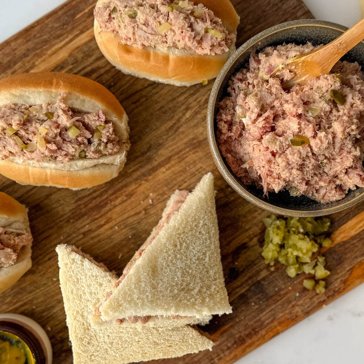 salade au jambon haché pour garniture à sandwich dans un bol avec petites sandwichs et cornichons hachés, sur une planche en bois