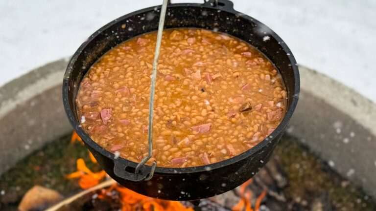 fèves au lard au jambon et à l'érable dans une grande cocotte en fonte sur le feu de camp