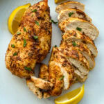 deux poitrines de poulet grillées, une coupée en tranche, avec quartiers de citron dans une assiette blanche