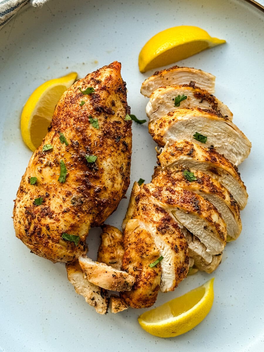 deux poitrines de poulet grillées, une en lanières. quartiers de citron dans une assiette blanche