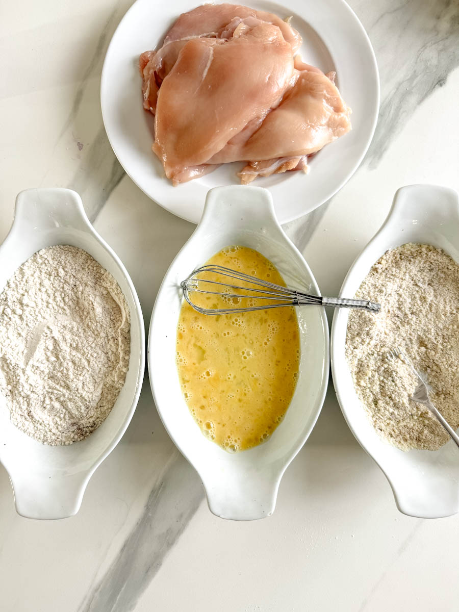 assiette avec escalopes de poitrines de poulet et trois plat: farine, oeuf battu et chapelure assaisonnée pour panure en trois temps