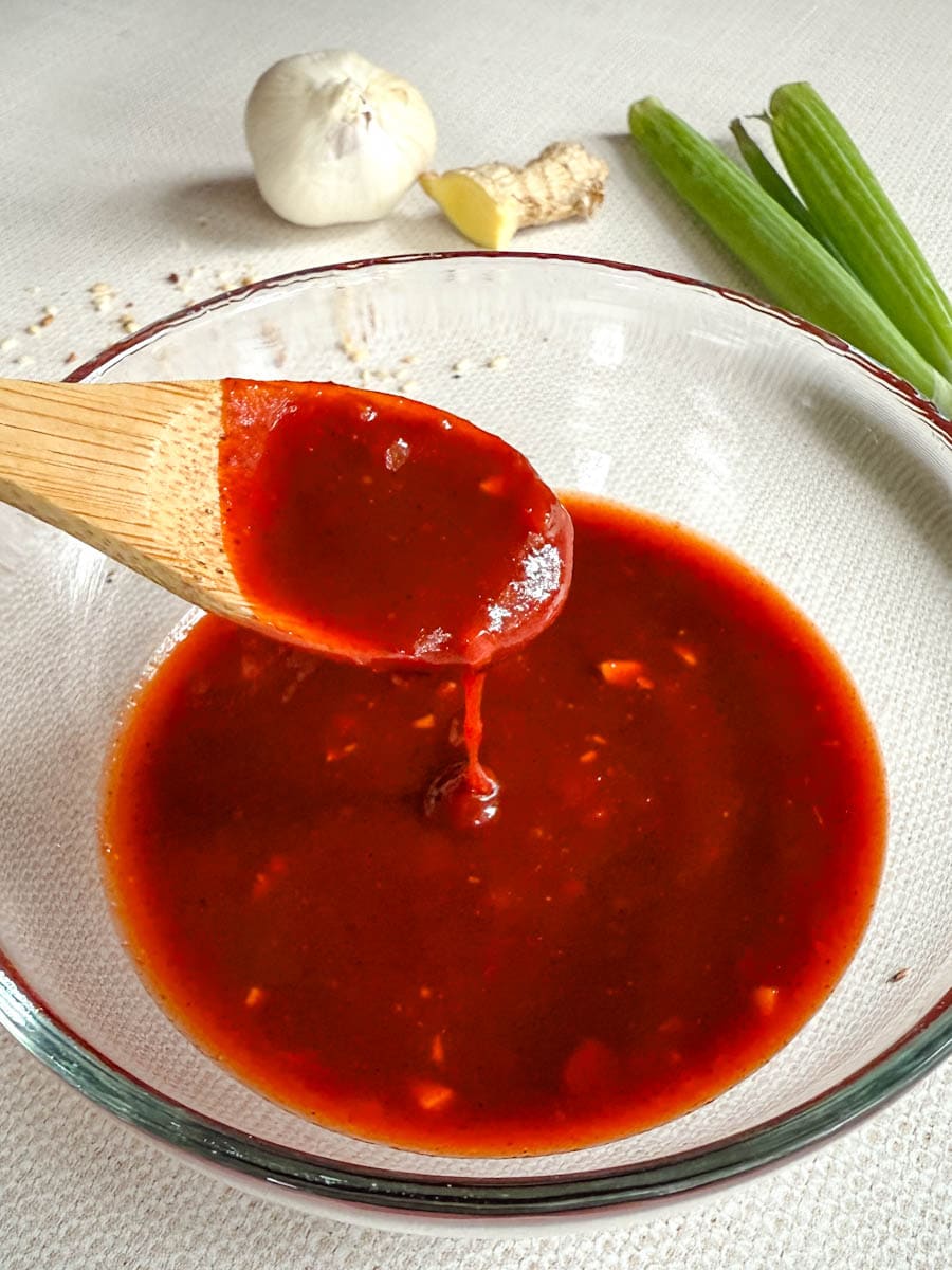 marinade gochujang dans un bol en verre avec ail, gingembre et oignons vert en arrière plan
