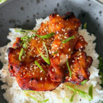 poulet gochujang grillé sur du riz avec oignon vert et graines de sésame dans un bol noir tacheté
