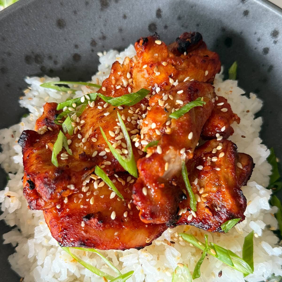 poulet gochujang grillé sur du riz avec oignon vert et graines de sésame dans un bol noir tacheté