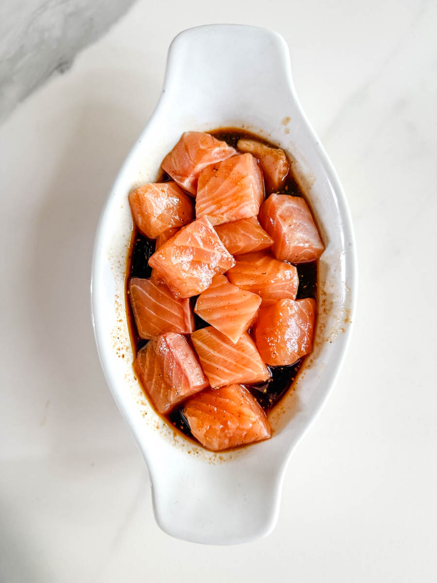 dés de saumon dans marinade foncée dans plat ovale blanc sur comptoir blanc marbré