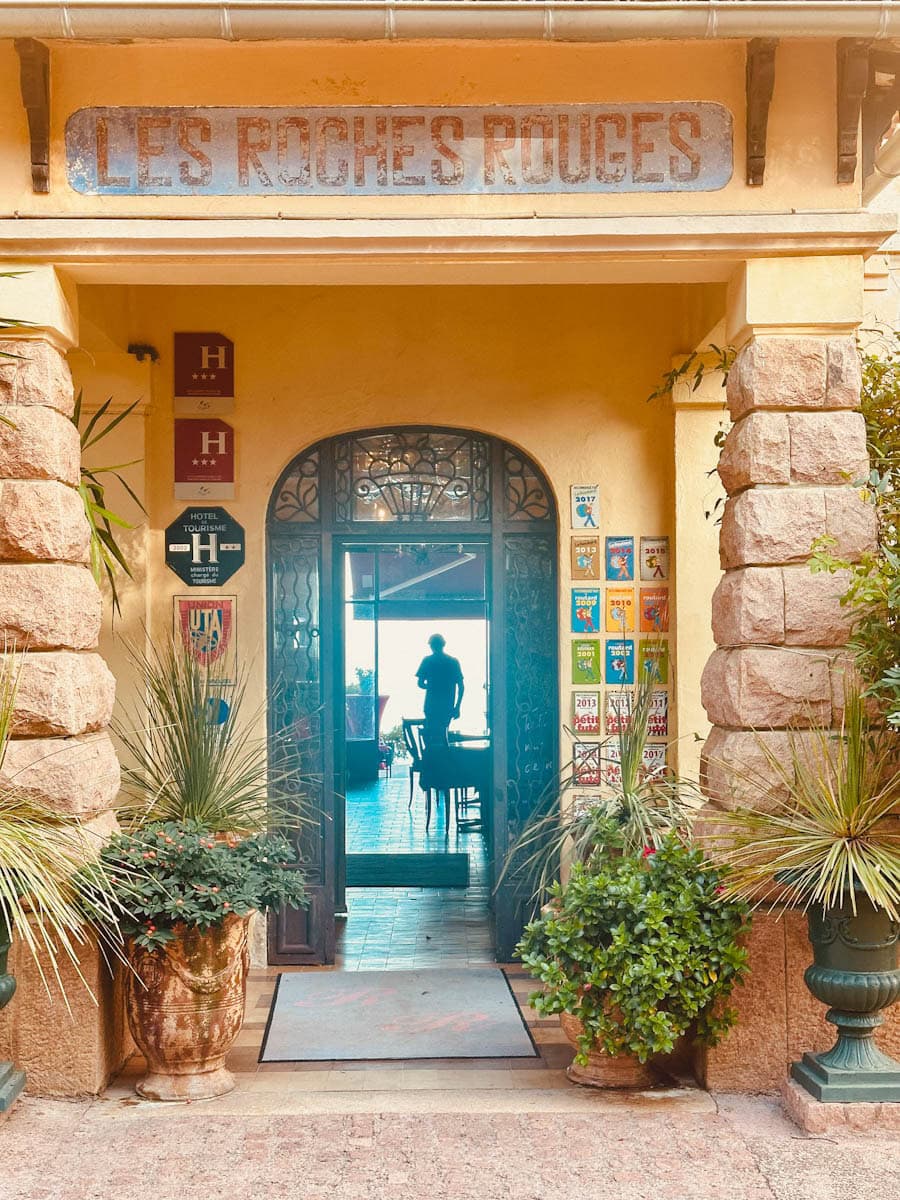 Entrée de l'hotel roches rouges avec panneau, personne en contrejour et plantes