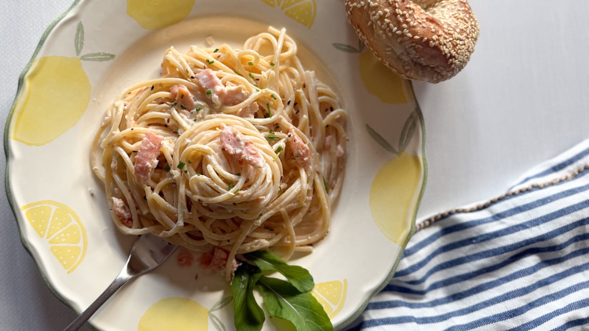 spaghetti au saumon fumé sauce crémeuse dans une jolie assiette décorée de citrons peints sur table blanche avec linge rayé et bagel sur le côté