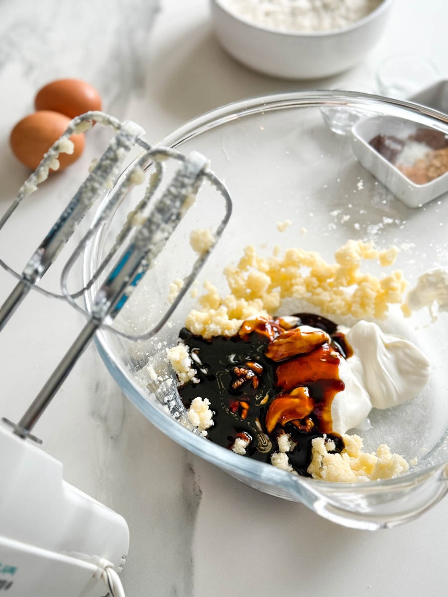 pate à muffin avec mélasse dans un bol en verre, batteur électrique et oeufs en arrière plan