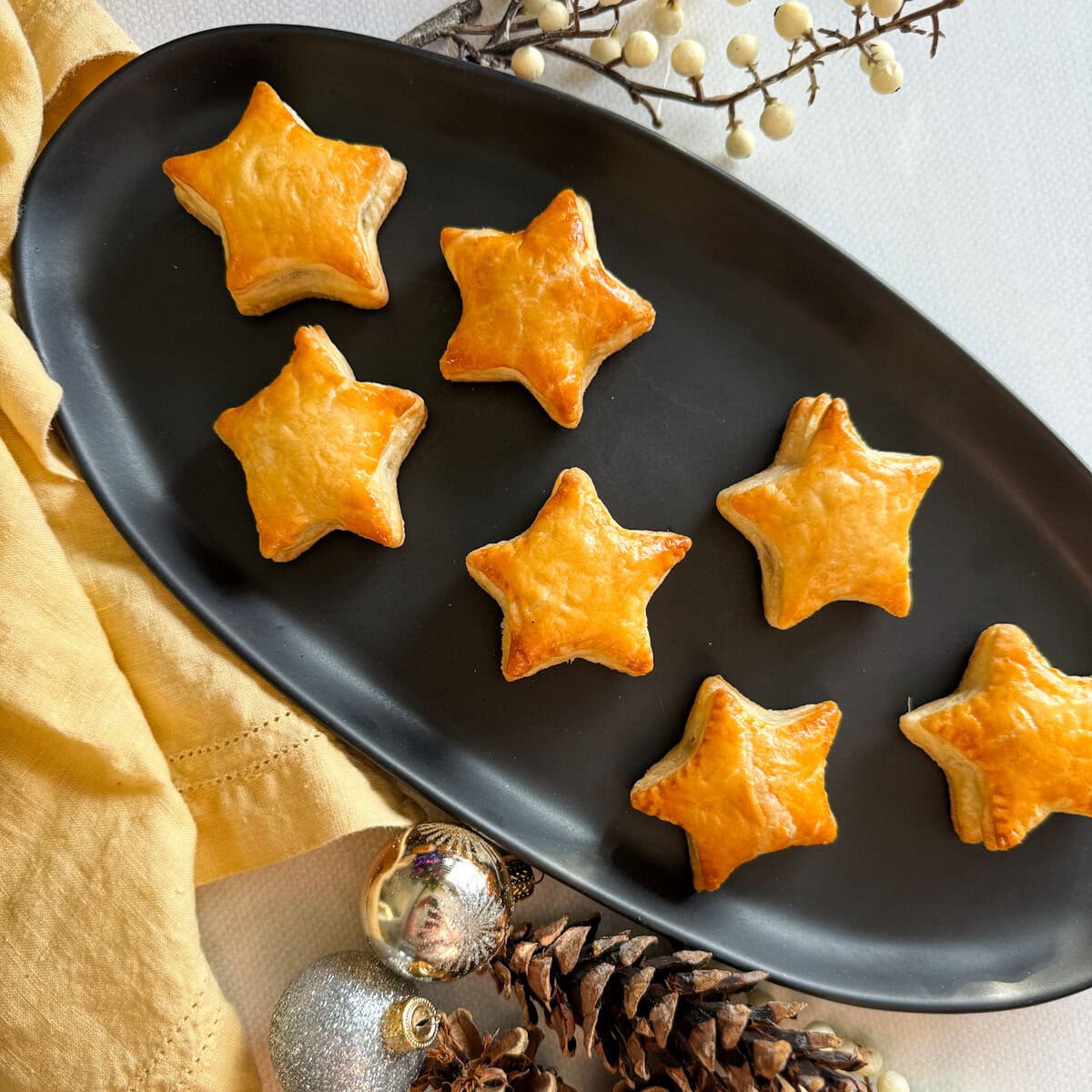 feuilletés festifs en forme d'étoile dans une assiette ovale noire avec décorations de noël et linge de table jaune