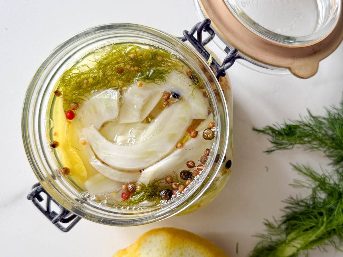 fenouil en marinade dans un pot en verre ouvert, avec citron et barbe de fenouill sur comptoir