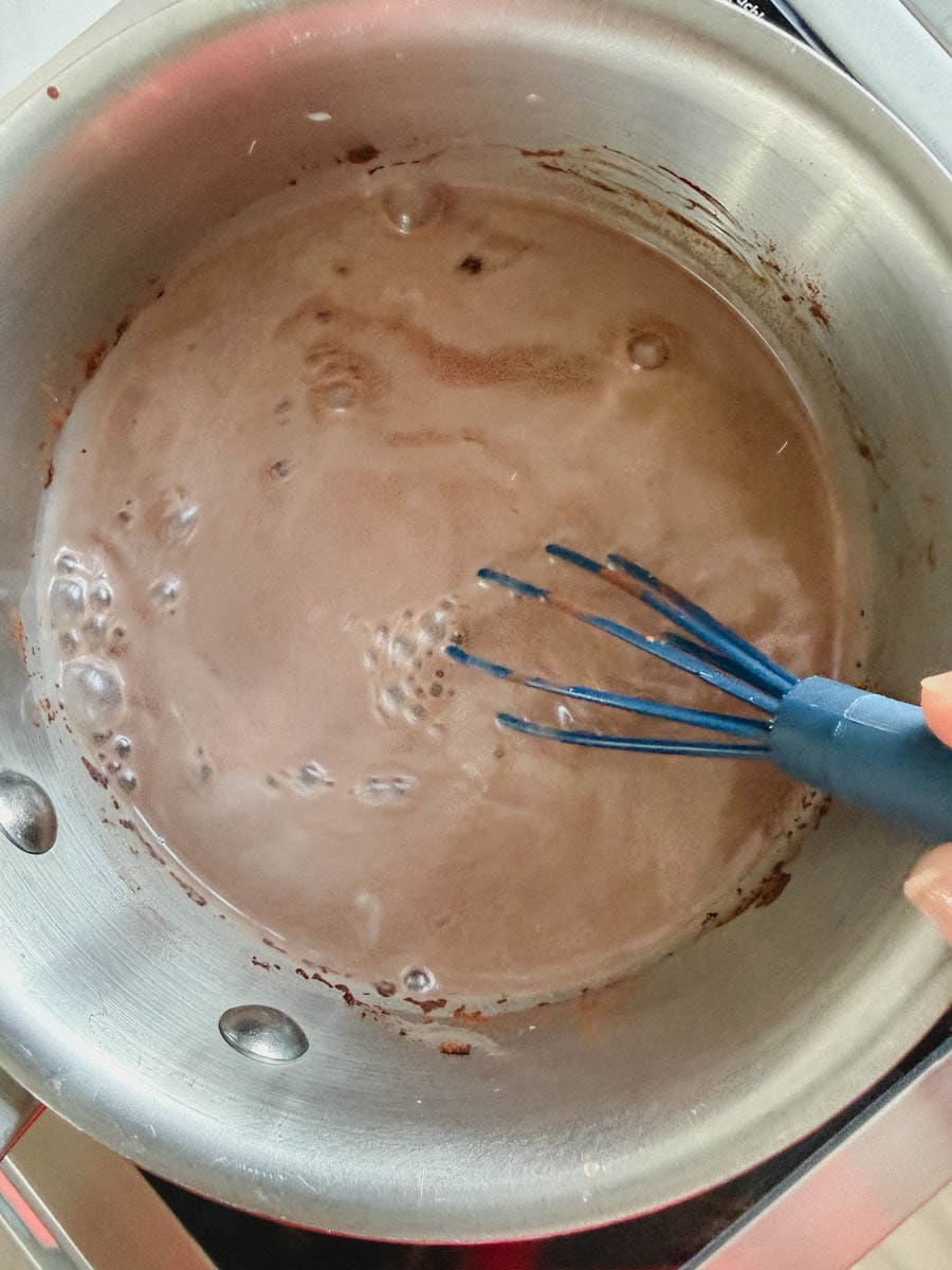 main qui tient fouet dans une casserole avec chocolat chaud maison