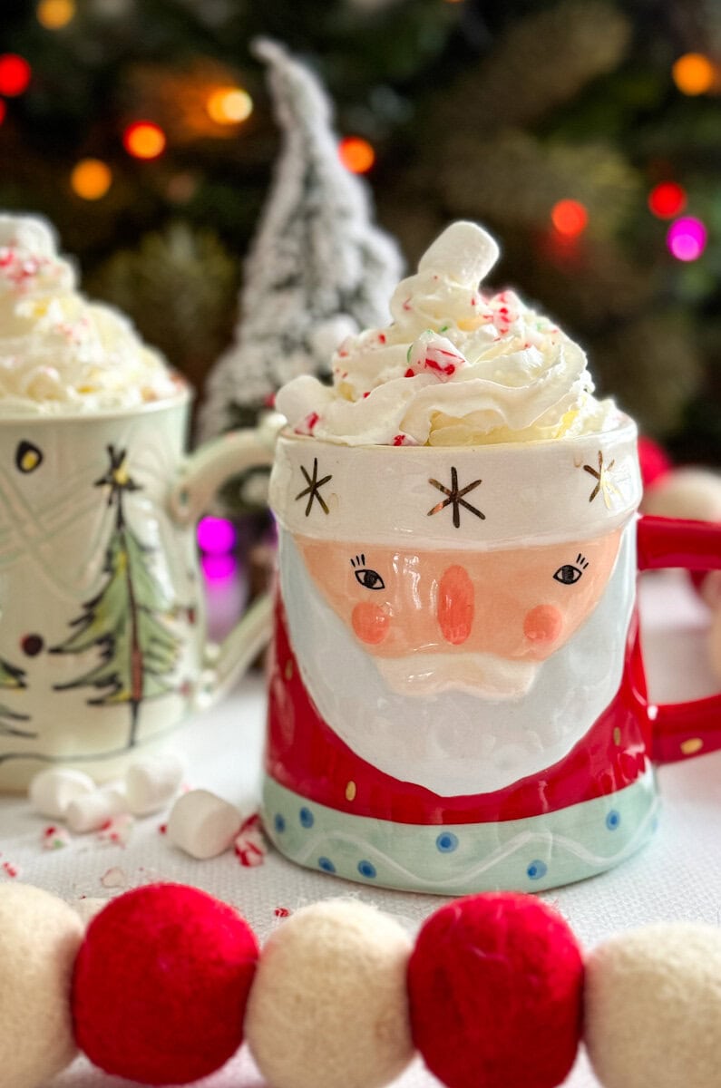 Tasse de père Noël et tasse avec sapins de Noël avec crème fouettée et canne de Noël devant décorations festives