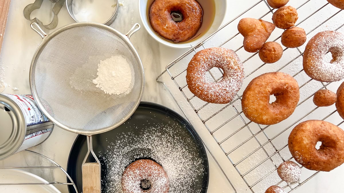 beignes aux patates, sucre à glacer, bol de sirop d'érable sur surface de travail