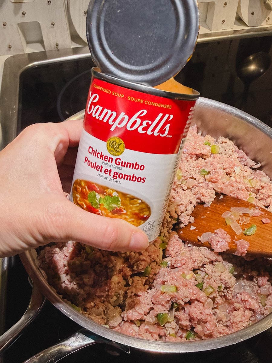 main tenant une boite de conserve Campbell's ouverte Soupe condensée Poulet et gumbos au dessus de casserole avec sauce à la viande