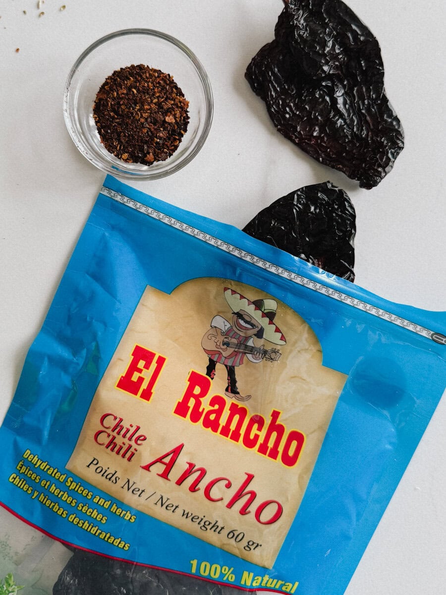sac de piments ancho (marque El Rancho) ouvert avec piments ancho sur comptoir et petit pot de piment ancho moulu