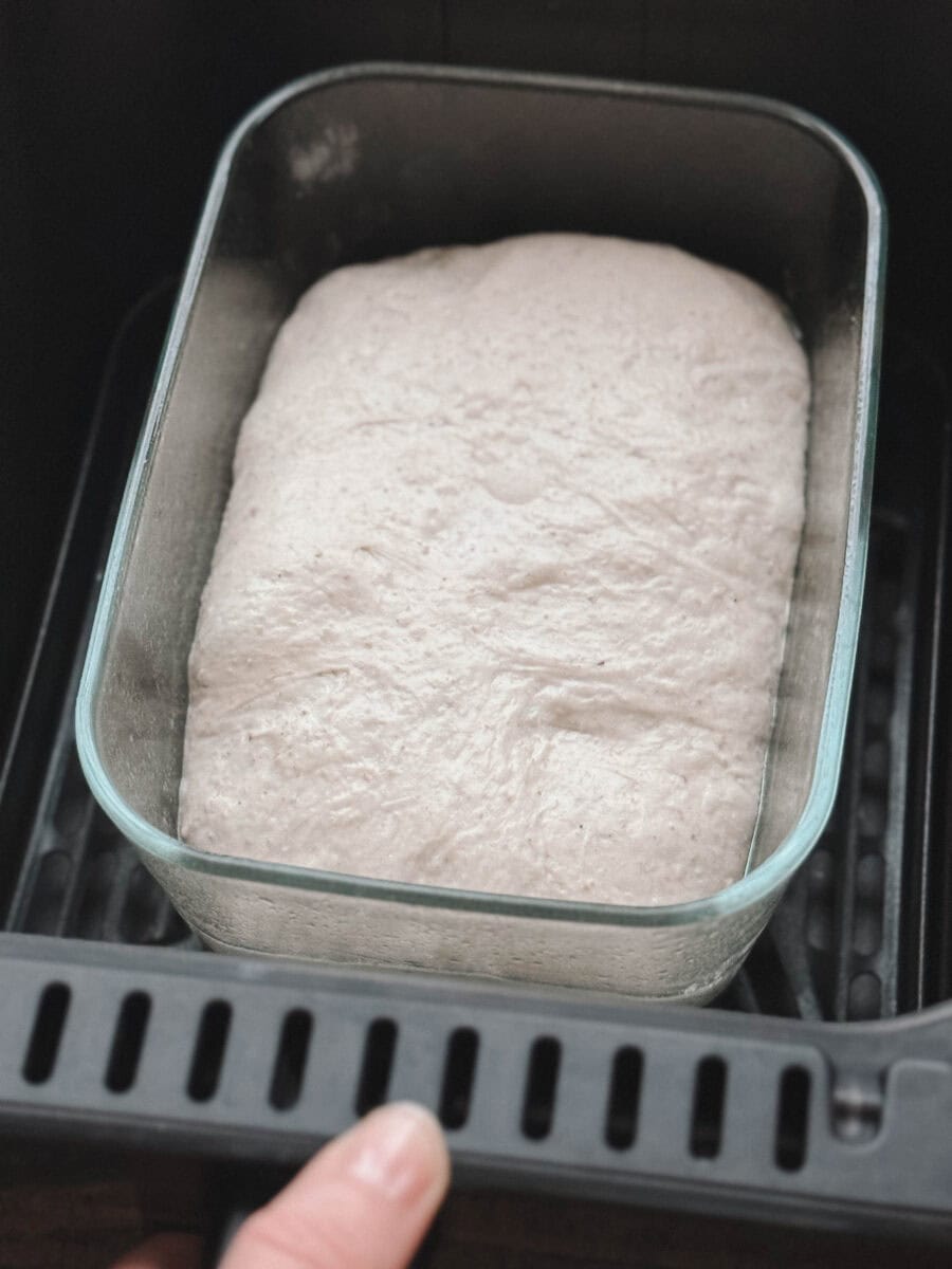 pain au levain dans un moule dans le panier du air fryer tenu par une main