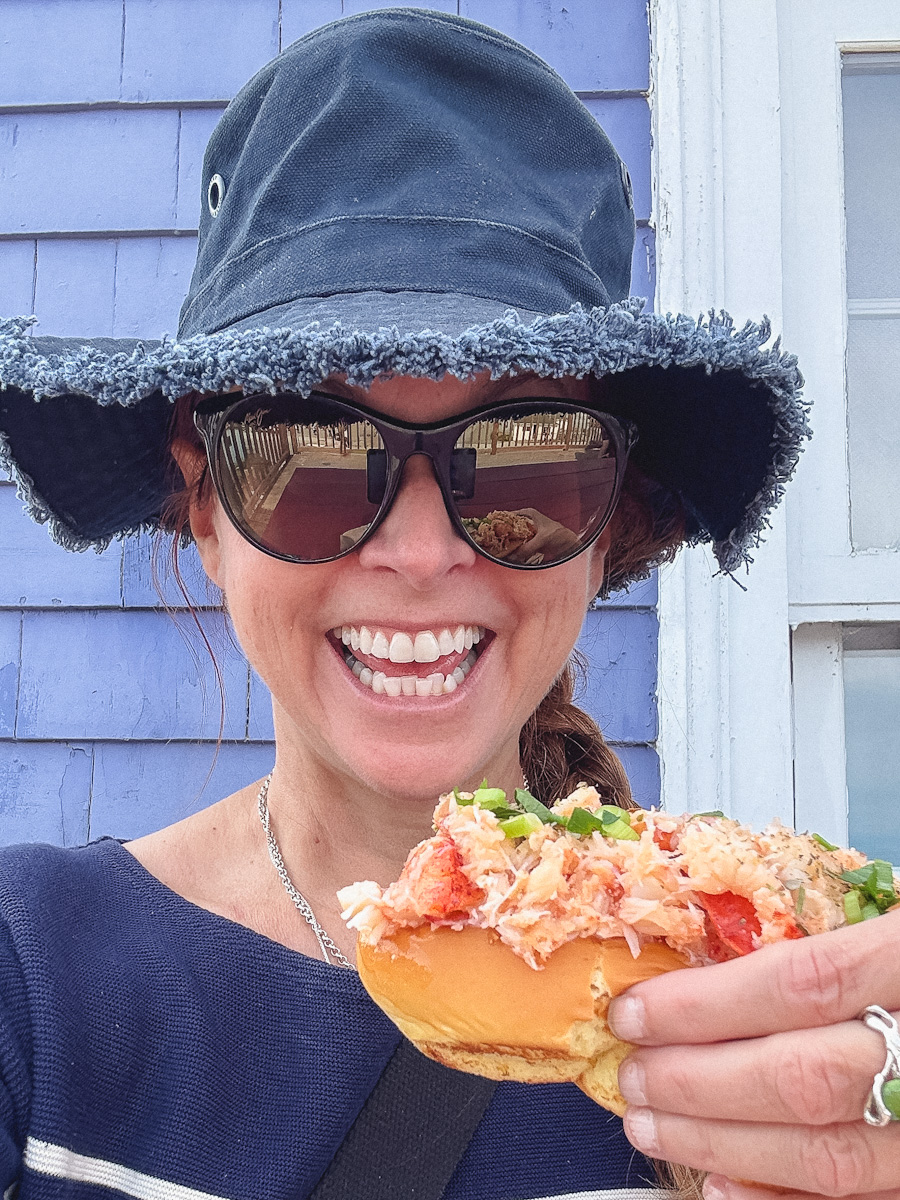 Manon Lapierre qui tient un lobster roll bien garni, tout sourire