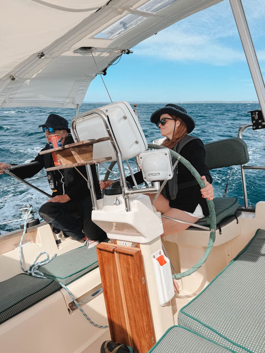 Manon Lapierre qui tient la barre d'un voilier avec capitaine à ses côtés