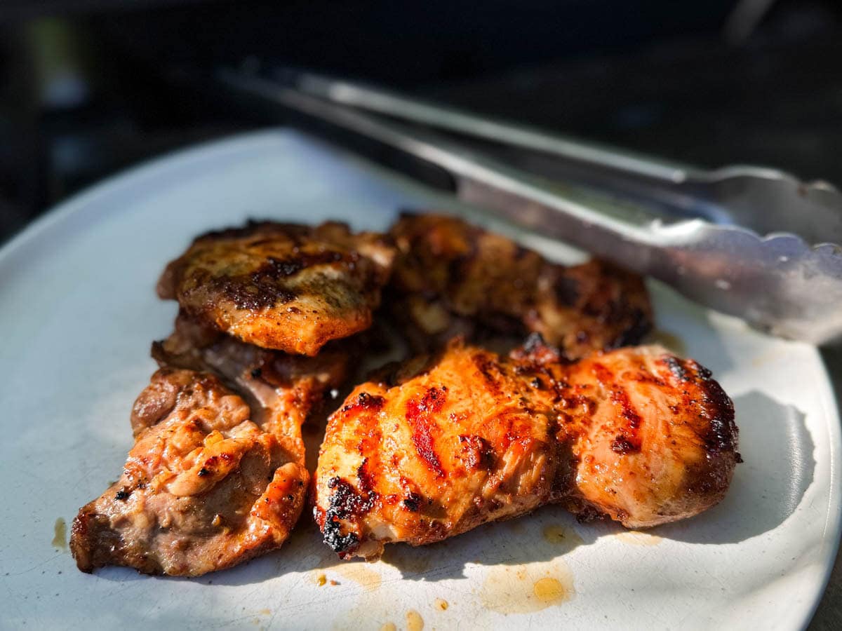 poulet chipotle grillé dans une assiette devant bbq avec pinces en métal