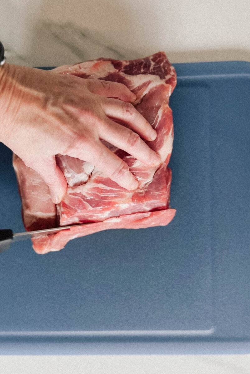 main qui coupe une longe de porc sur planche bleue