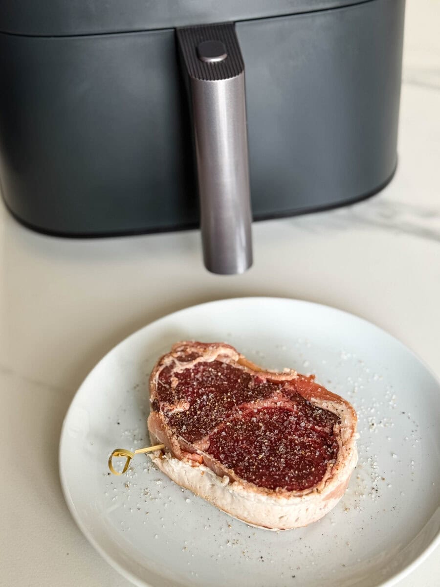 tournedos de boeuf bardé de bacon, non cuit, salé poivré dans assiette blanche devant tiroir de l'air fryer